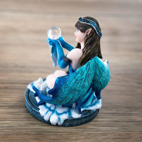 Figurine of brunette fairy in blue dress sitting in snow by a crystal cluster, holding crystal ball