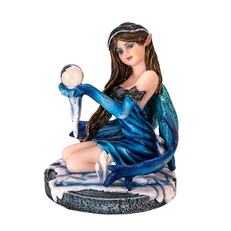 Figurine of brunette fairy in blue dress sitting in snow by a crystal cluster, holding crystal ball