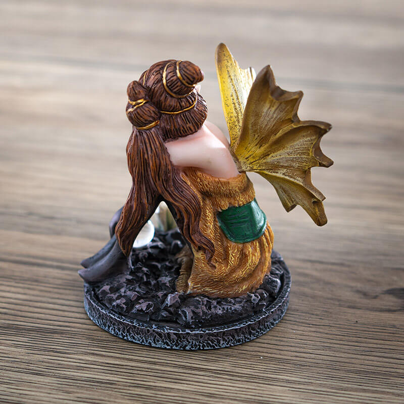 Figurine of a fairy in a gold and green dress with yellow wings, black stockings and gloves. Sitting with a crystal ball and crystal cluster. Elaborate brunette hairdo.