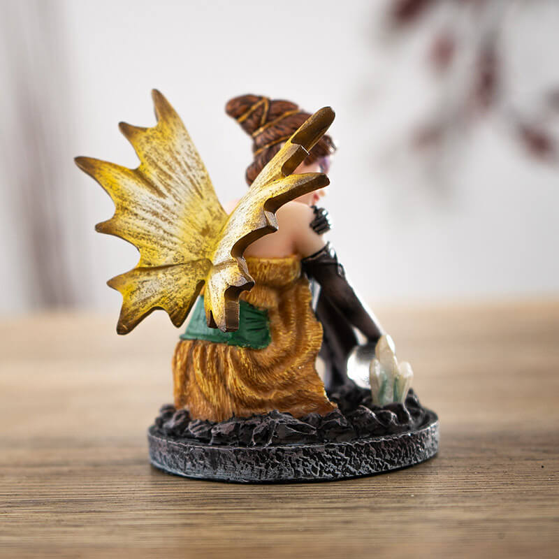 Figurine of a fairy in a gold and green dress with yellow wings, black stockings and gloves. Sitting with a crystal ball and crystal cluster. Elaborate brunette hairdo.