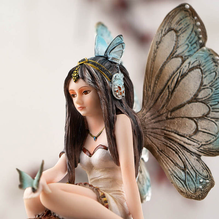 Figurine of brunette fairy with tan and brown wings and cream dress sitting on mushroom with butterfly on her hand, more toadstools below.