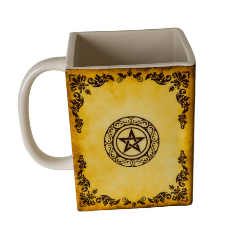 Square mug in yellow/tan with black, "Grimoire" and "Book of Spells" written with moon and pentacle, leaf designs