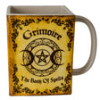 Square mug in yellow/tan with black, "Grimoire" and "Book of Spells" written with moon and pentacle, leaf designs