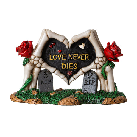 Figurine of skeleton hands forming heart with roses and gravestones, text reading "LOVE NEVER DIES"