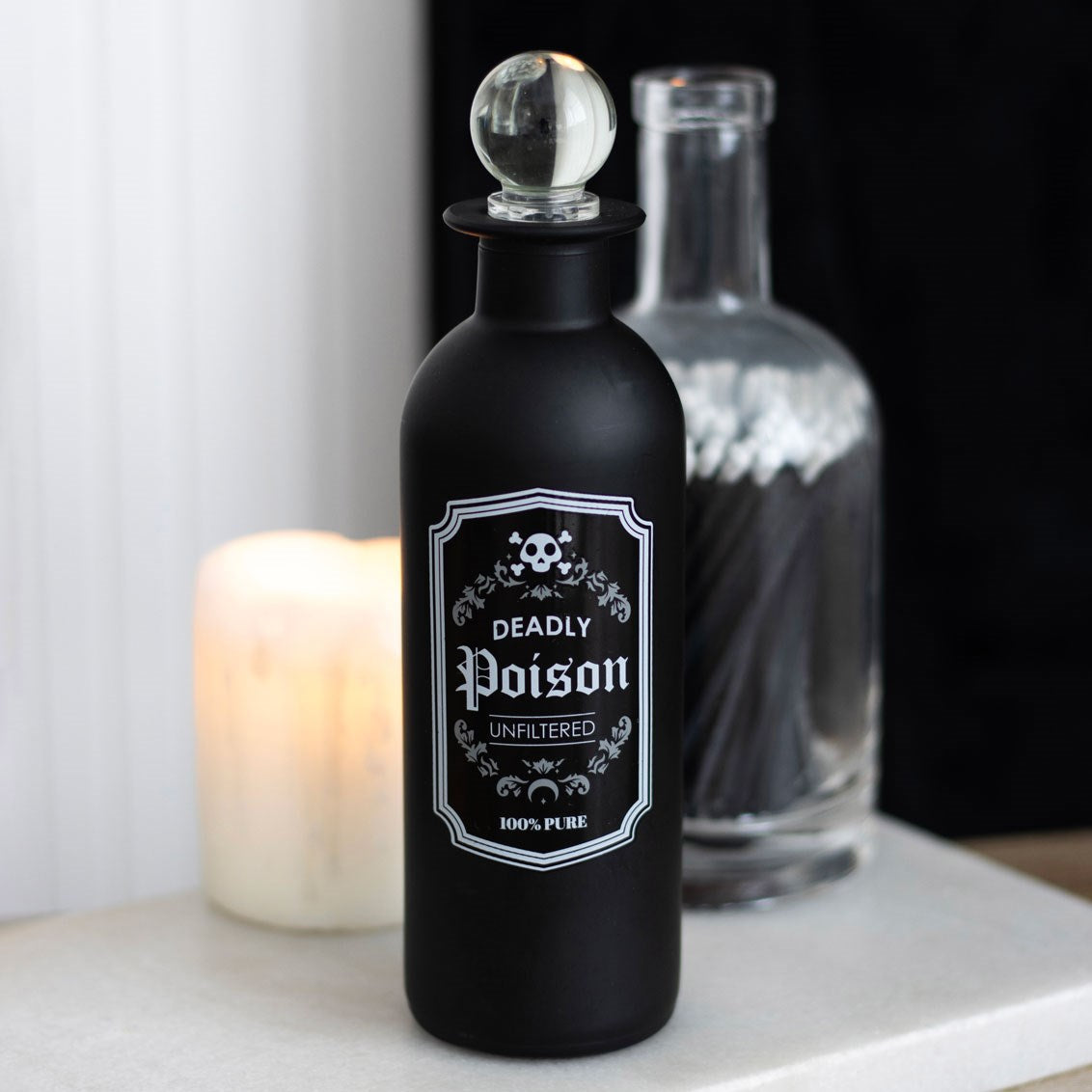 Decorative glass bottle, black with "Deadly Poison, Unfiltered, 100% Pure" label and clear glass stopper
