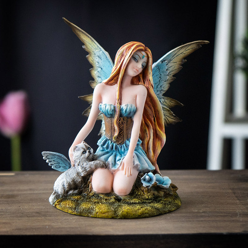 Figurine of blond fairy with blue wings and blue and brown corset dress kneeling on moss with winged white cat