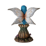 Figurine of fairy with blue hair and tan wings holding blue flower bouquet, sitting on mushroom , shown from the back