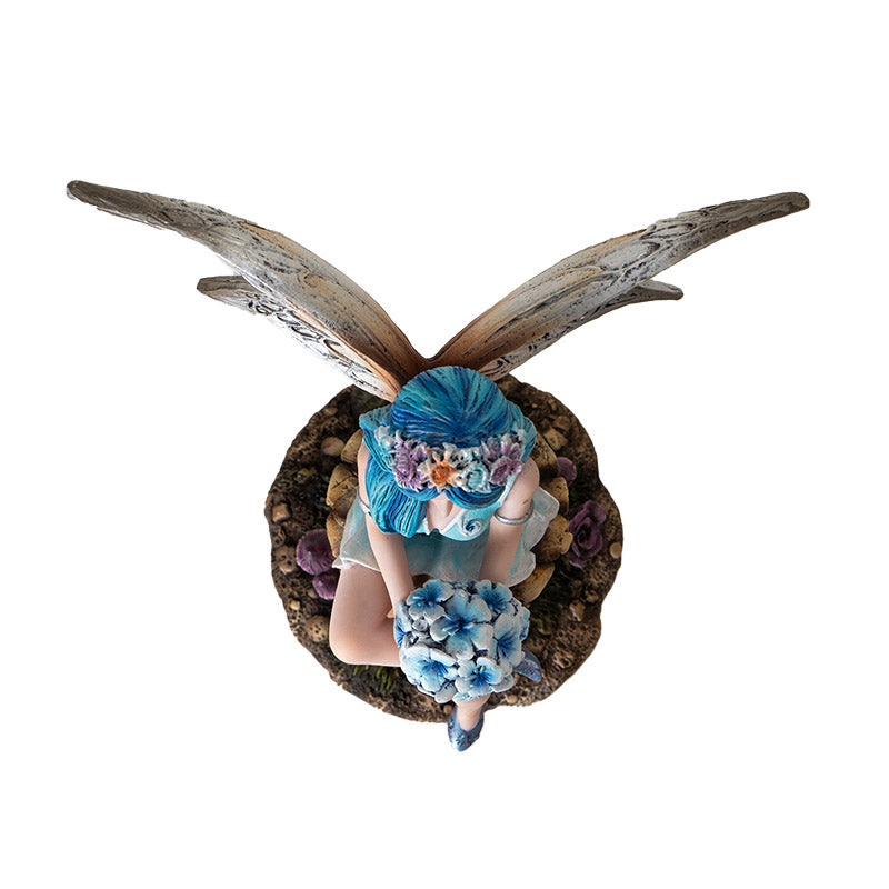 Figurine of fairy with blue hair and tan wings holding blue flower bouquet, sitting on mushroom , shown top down