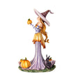 Figurine of a witch in pale purple and orange, holding up a pumpkin with more gourds at her feet and a black rabbit