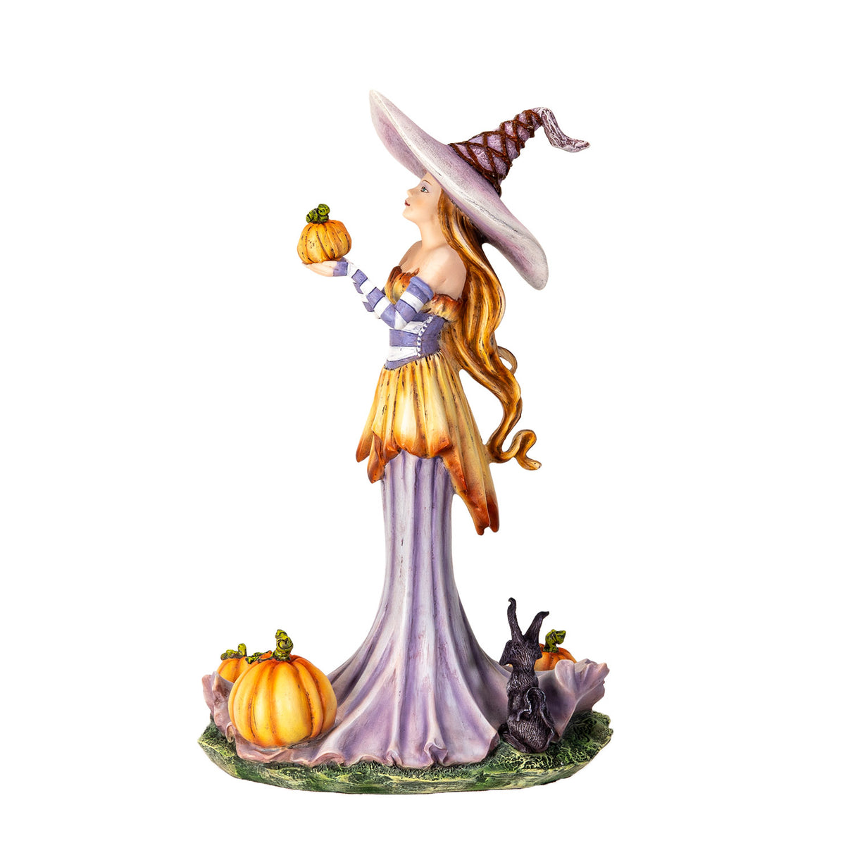 Figurine of a witch in pale purple and orange, holding up a pumpkin with more gourds at her feet and a black rabbit