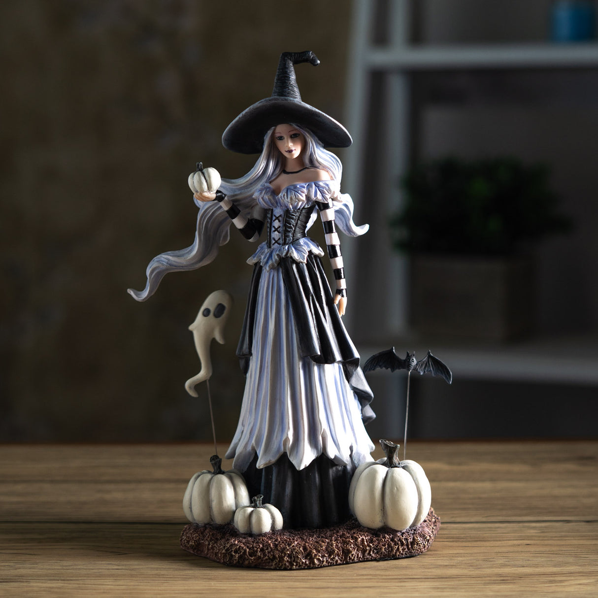 Halloween-themed figurine of a witch with white pumpkins and a ghost and bat