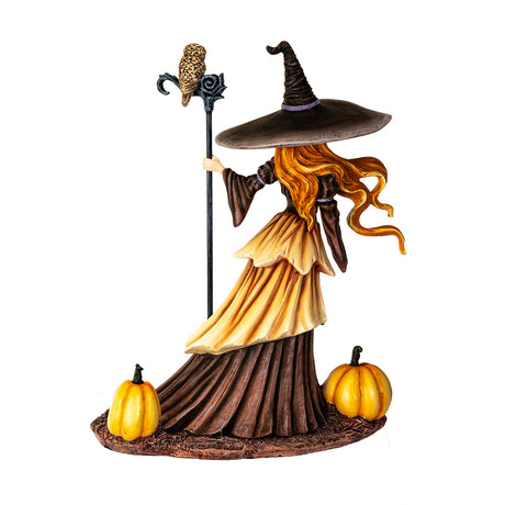 Figurine of witch with red hair, brown dress, surrounded by pumpkins, owl perched on her staff, shown from the back