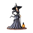 Figurine of a witch in a moody dress and big hat, her hair billowing in an unseen breeze. Next to her is a festive pumpkin, and perched upon it and on her hat are ravens