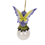 Fairy ornament with purple hair and striped pants sitting on a clear glass ball. Purple and yellow wings, gazing out. Shown from the back