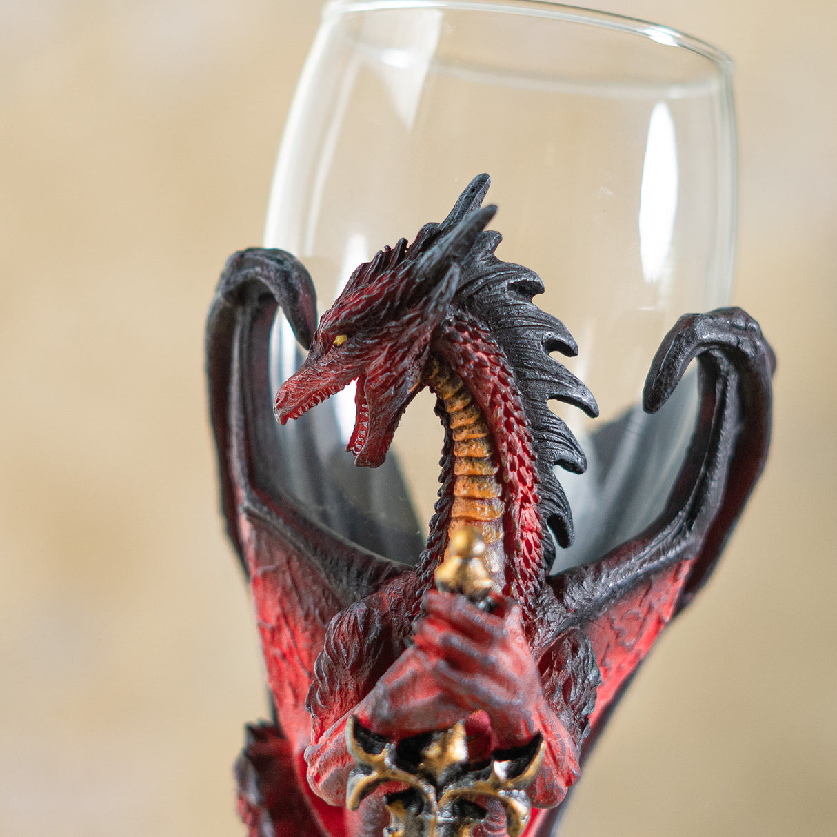 Closeup of red and black dragon holding sword, glass goblet