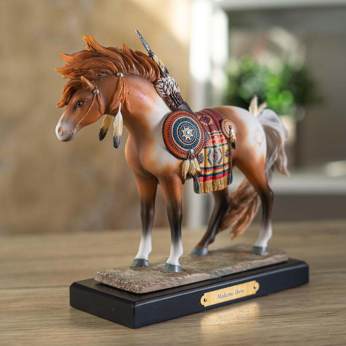 A decorative figurine of a horse standing on a black base with a gold plaque reading 'Medicine Horse.' The horse is a chestnut and white pinto with a multicolored saddle blanket and feather details in a Native American style