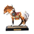 A decorative figurine of a horse standing on a black base with a gold plaque reading 'Medicine Horse.' The horse is a chestnut and white pinto with a multicolored saddle blanket and feather details in a Native American style