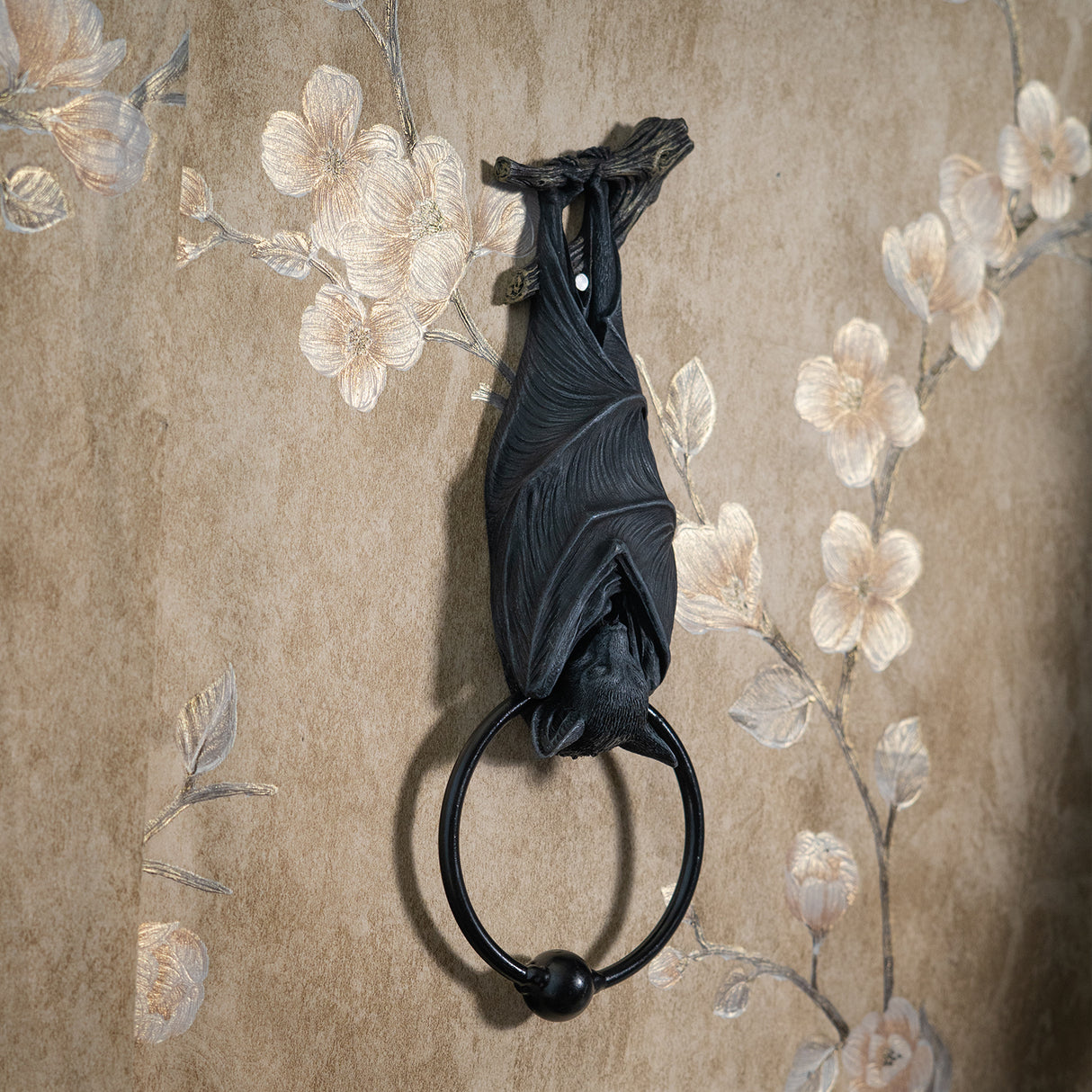 A black bat door knocker featuring a detailed bat sculpture hanging from a branch, with a circular ring at the bottom