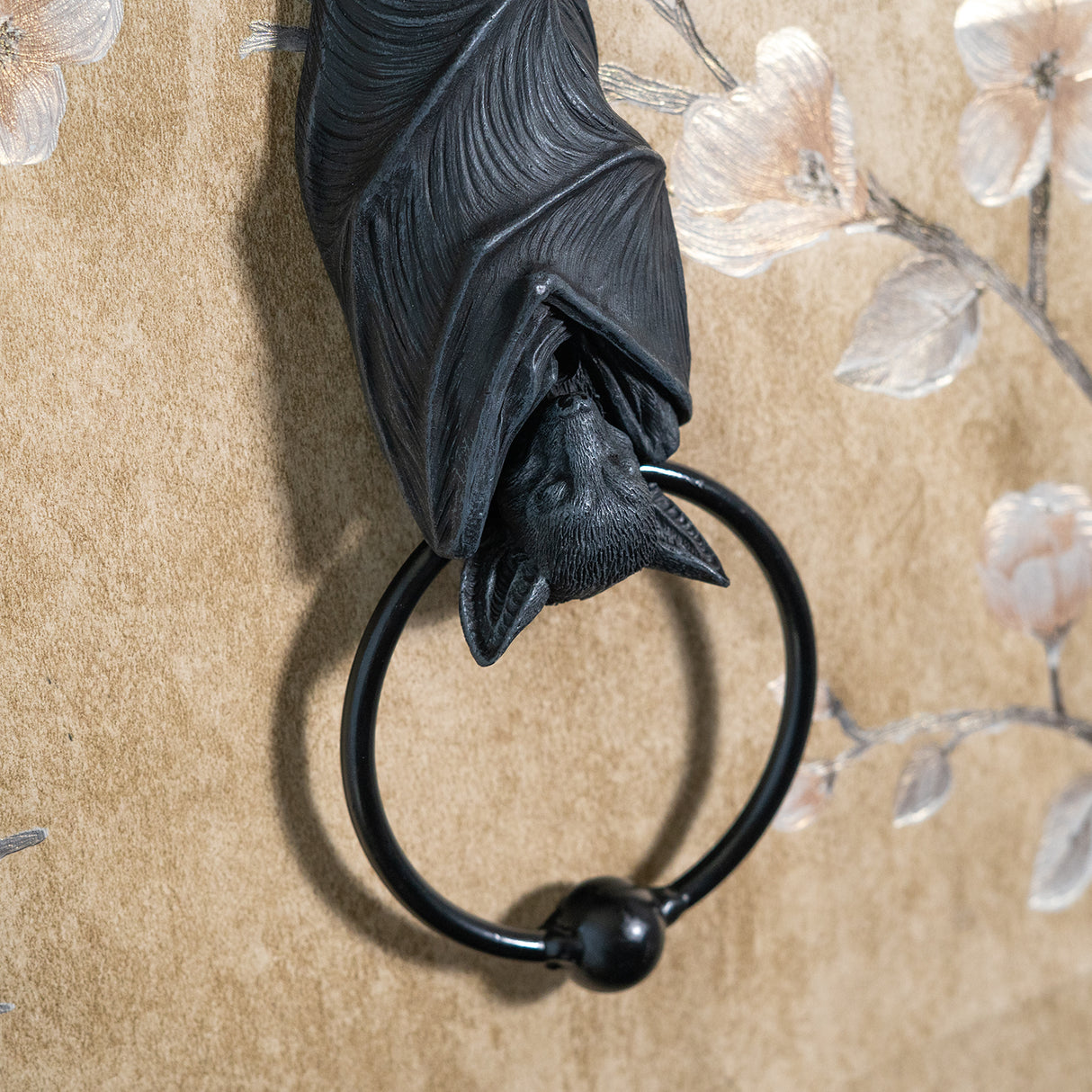 A black bat door knocker featuring a detailed bat sculpture hanging from a branch, with a circular ring at the bottom