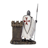 A medieval Templar knight figurine in chainmail and white shield with a red cross, holding a spear next to a small stone castle tower  that doubles as a utility desk caddy/pen holder, shown from the back