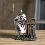 A medieval Templar knight figurine in chainmail and white surcoat with a red cross, holding a spear next to a small stone castle tower  that doubles as a utility desk caddy/pen holder