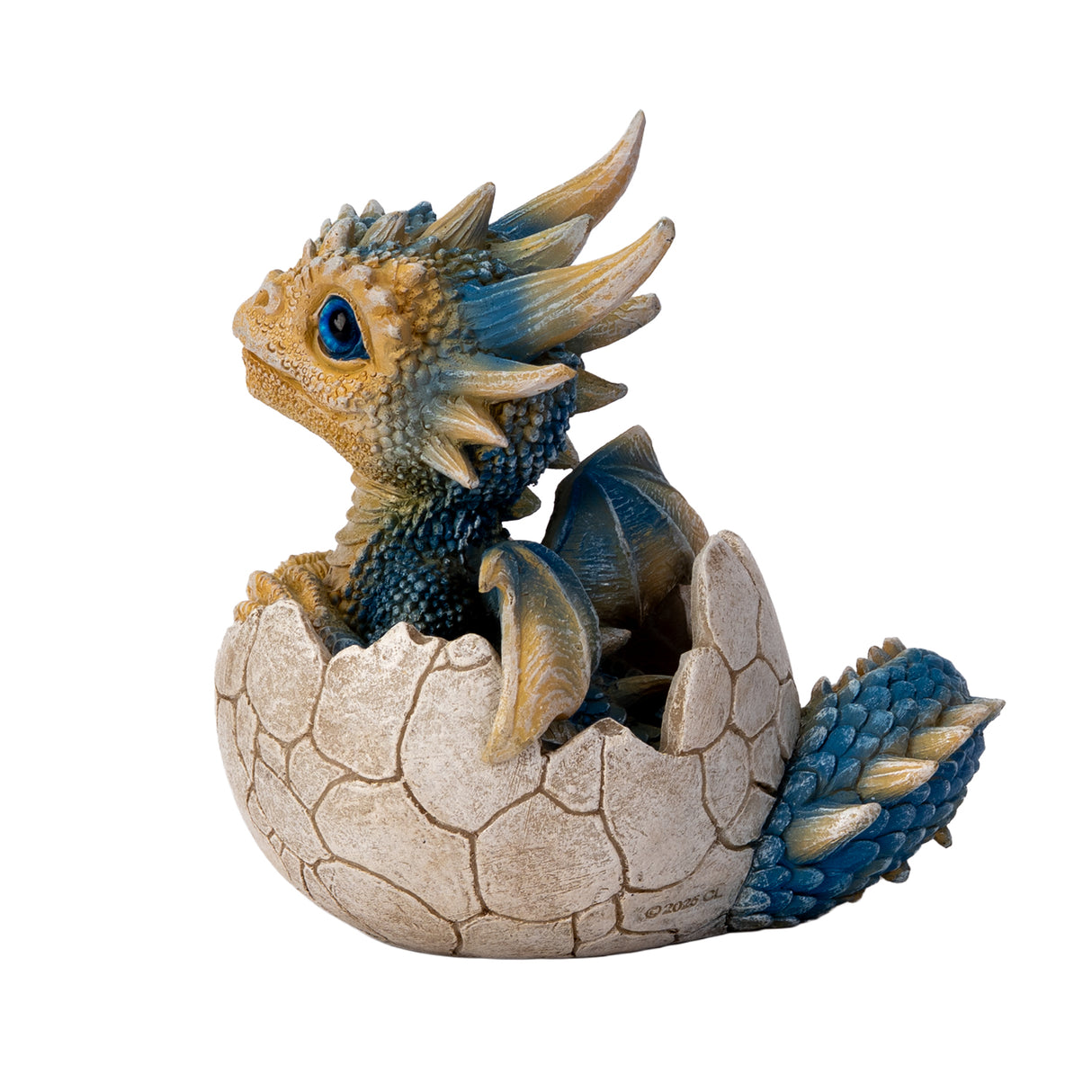 A small fantasy dragon figurine peeking out of a cracked eggshell, shown on a plain white background. The dragon has tan and blue scales, large bright blue eyes, black claws, and small wings. Shown from the side