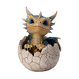 A small fantasy dragon figurine peeking out of a cracked eggshell, shown on a plain white background. The dragon has tan and blue scales, large bright blue eyes, black claws, and small wings.