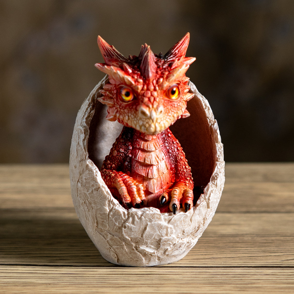 A small red dragon figurine sitting inside a cracked stone egg