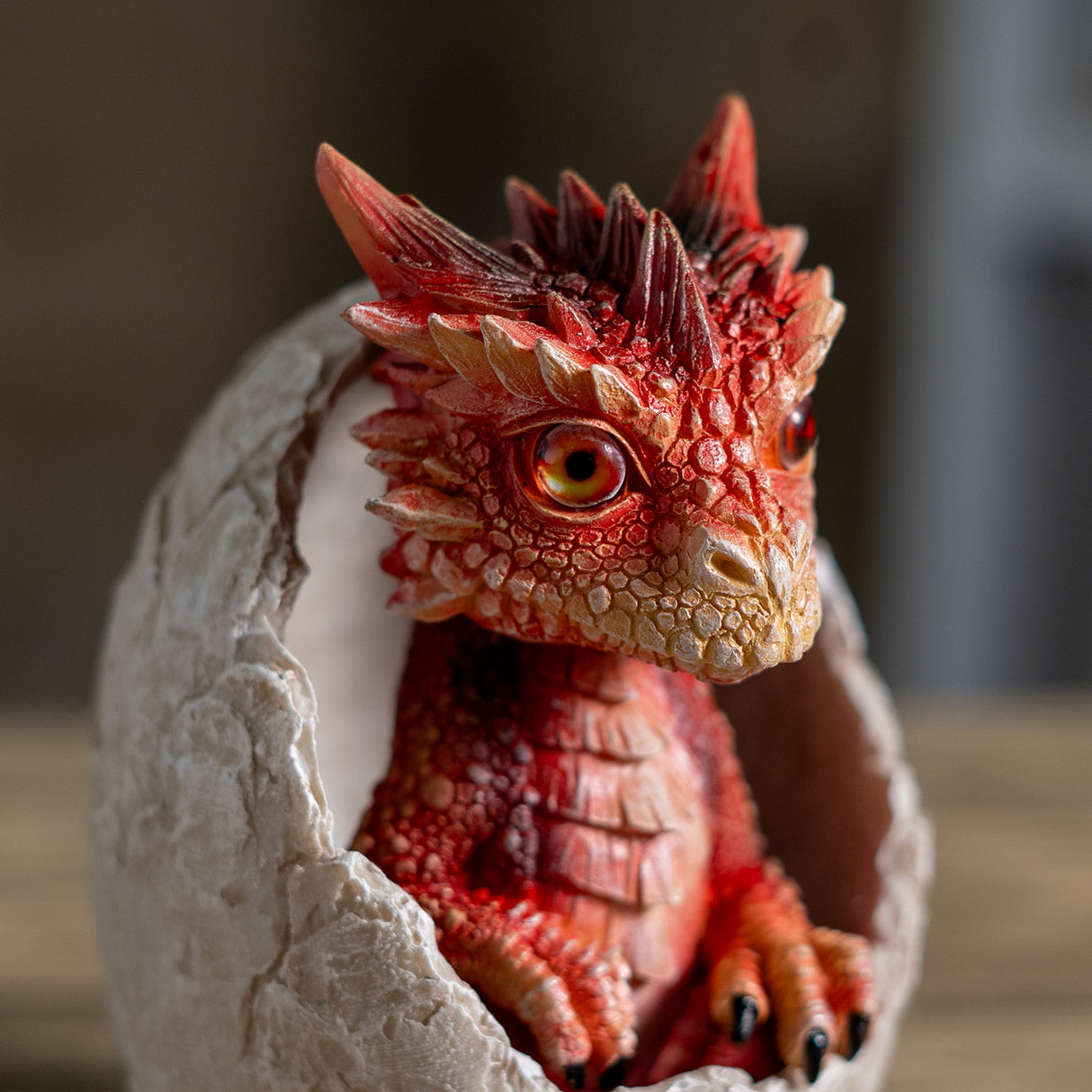 A small red dragon figurine sitting inside a cracked stone egg