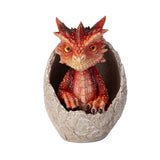 A small red dragon figurine sitting inside a cracked stone egg