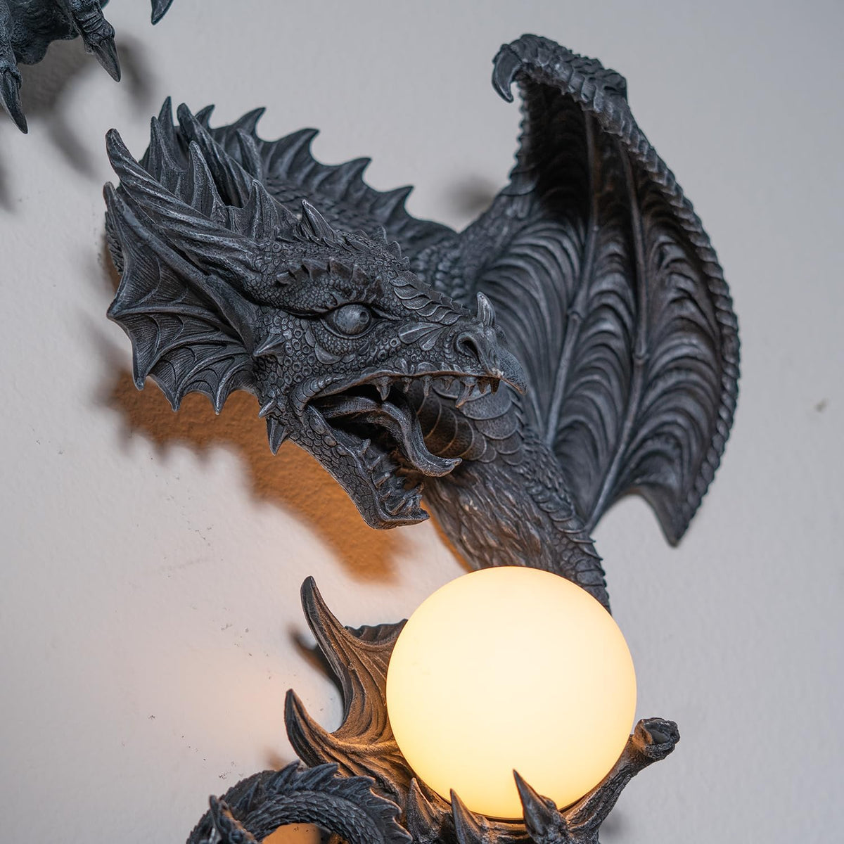 Dark gray faux-stone wall mounted lamp shaped like a dragon with an orb that glows