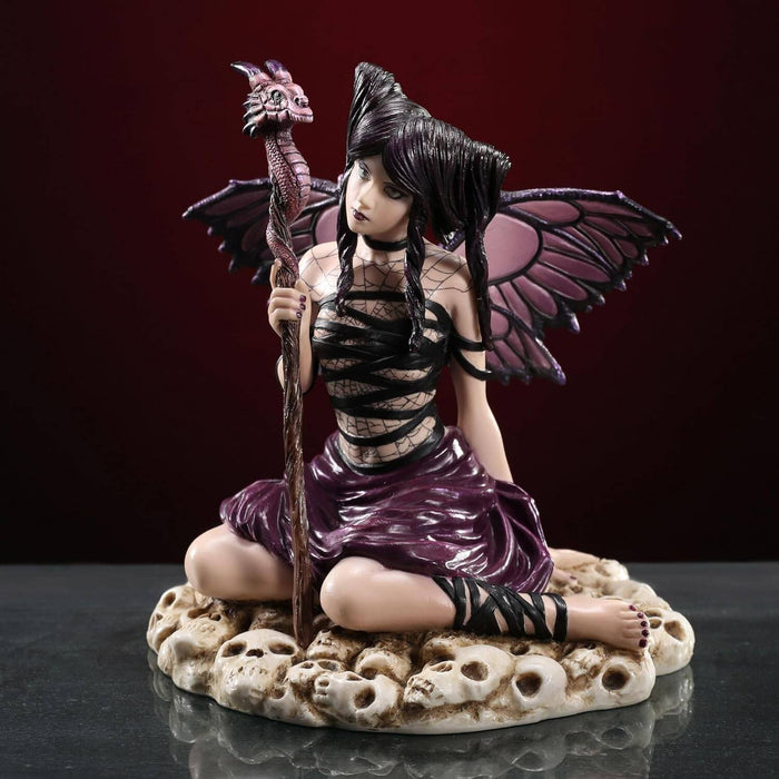 Fairy figurine of pixie with purple and black wings and outfit holding a dragon staff and sitting on skulls