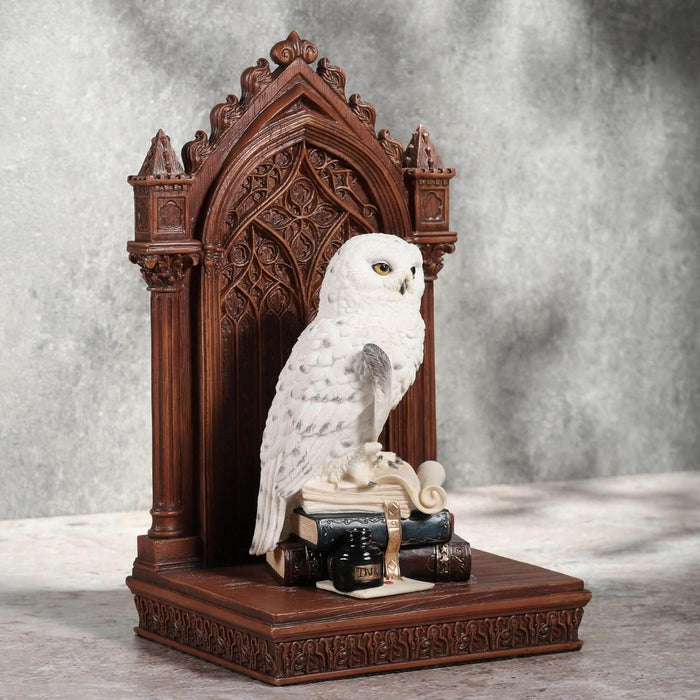 Snowy owl with golden eyes on bookstack holding quill, with faux-wood beyond