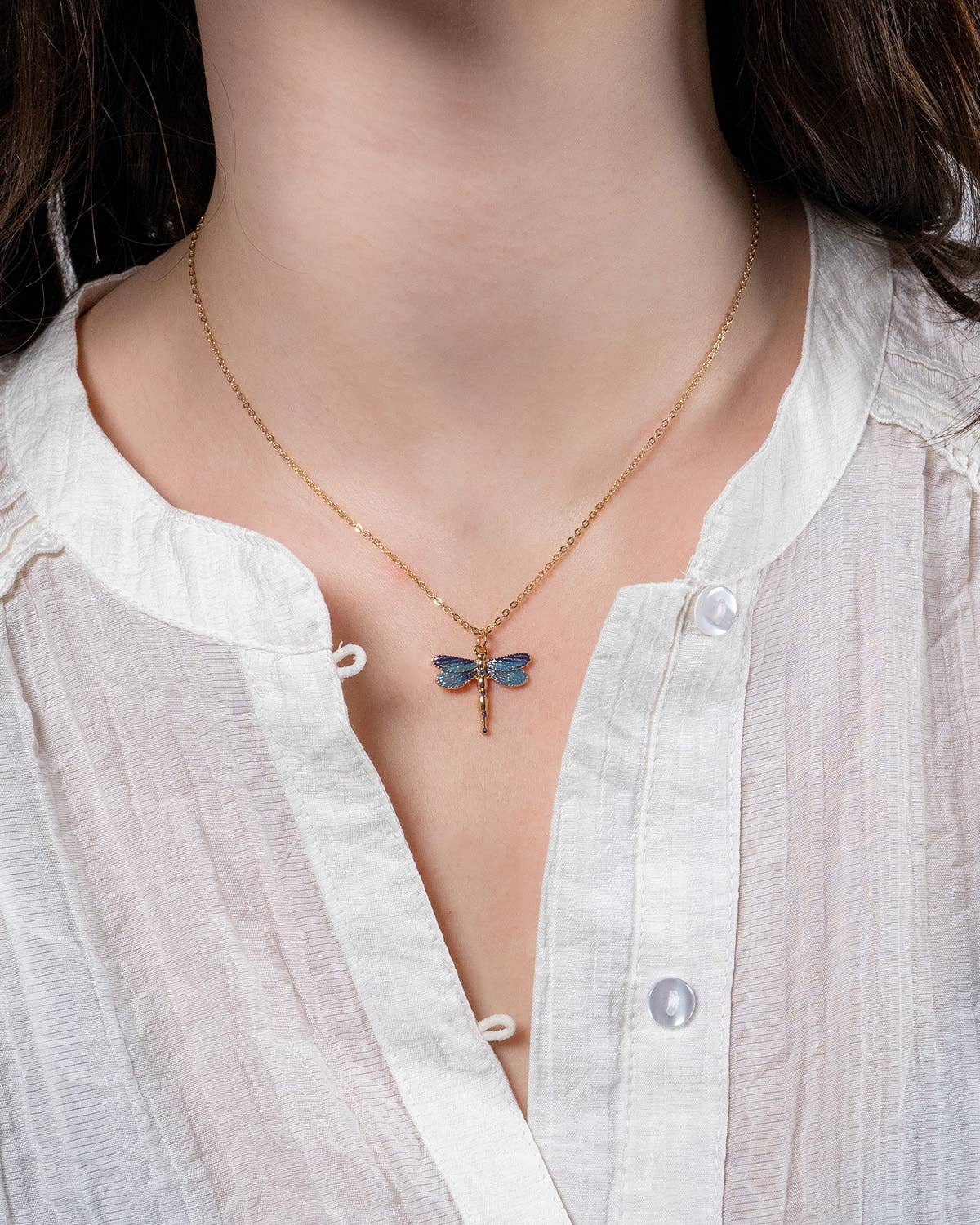 Necklace with a blue butterfly pendant worn by a person in a white shirt.