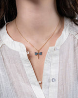Necklace with a blue butterfly pendant worn by a person in a white shirt.