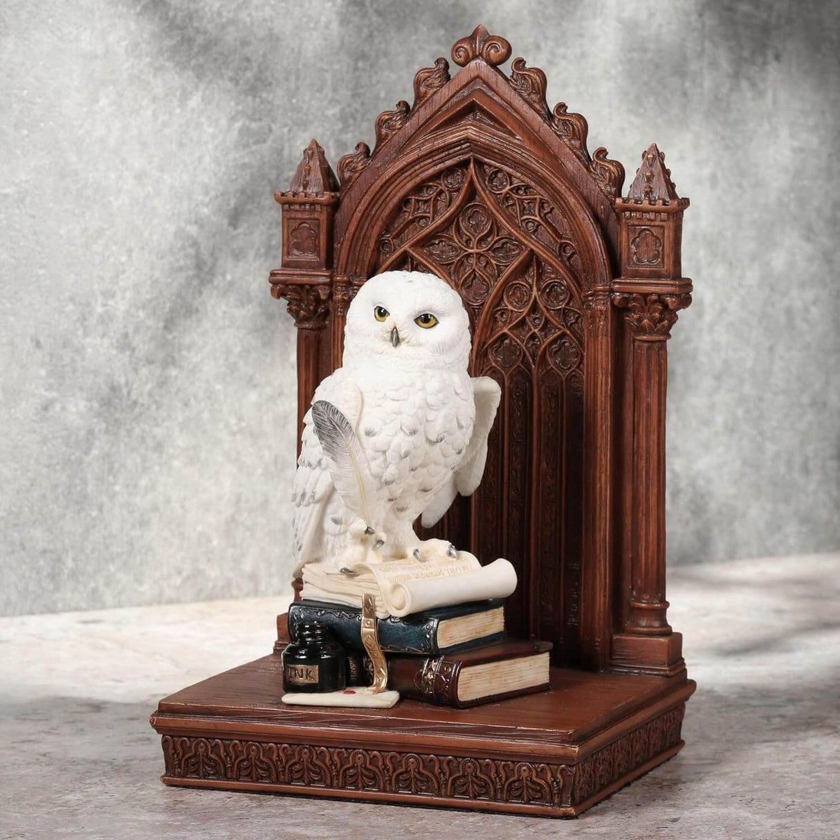 Snowy owl with golden eyes on bookstack holding quill, with faux-wood beyond