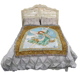Tapestry blanket with an angel and doves surrounded by an elaborate floral border, shown on a bed