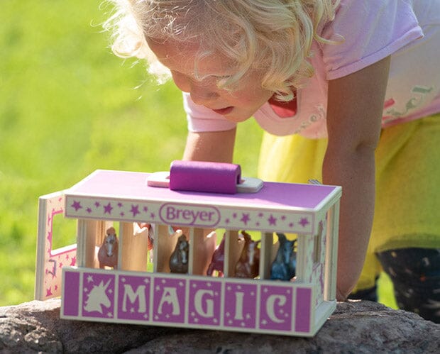 Breyer toy horse carrier with unicorn figurines, "MAGIC" written across the front, pink on wood, shown with a little girl
