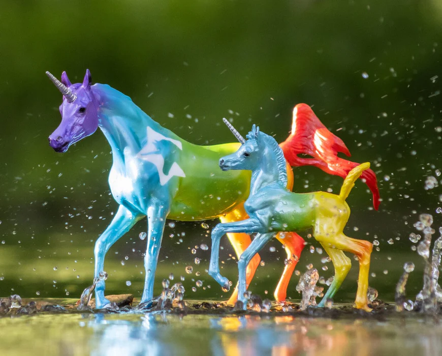 Two rainbow-colored unicorn figurines, mare and foal, running through water
