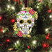 Colorful sugar skull skeleton ornament with red flowers and swirl designs and leaves, shown on a tree