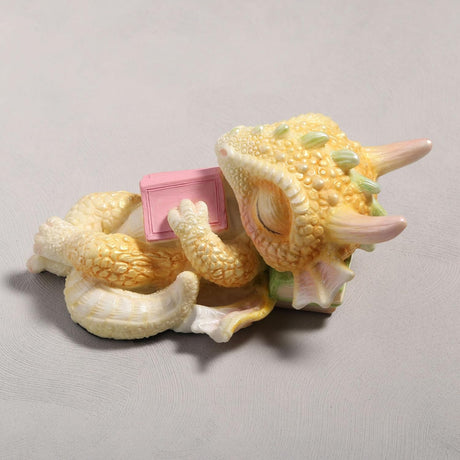 Cute sleeping dragon figurine holding a pink book