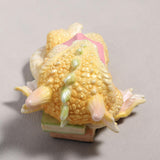 Cute sleeping dragon figurine holding a pink book, shown from the top, books under his head