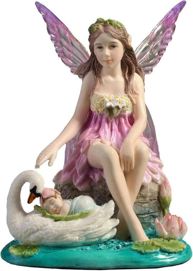 Fairy figurine with pink dress and wings sitting next to a swan with a baby on its back, surrounded by water lilies.