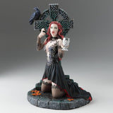 Gothic figurine of a vampire woman with red hair holding a goblet in front of a Celtic cross with a raven perched upon it