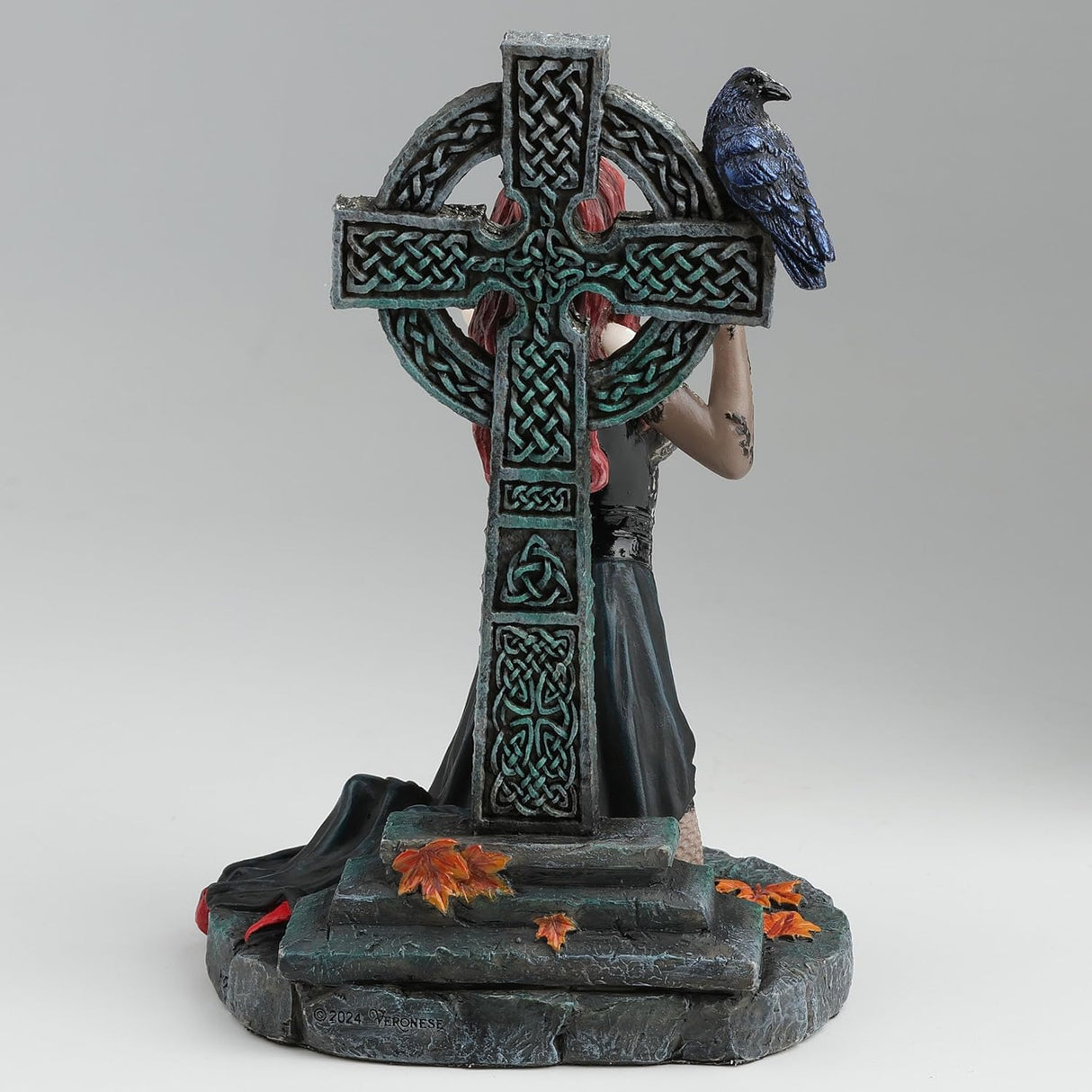 Gothic figurine of a vampire woman with red hair holding a goblet in front of a Celtic cross with a raven perched upon it, shown from the back