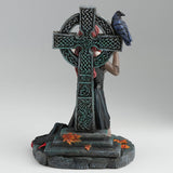 Gothic figurine of a vampire woman with red hair holding a goblet in front of a Celtic cross with a raven perched upon it, shown from the back