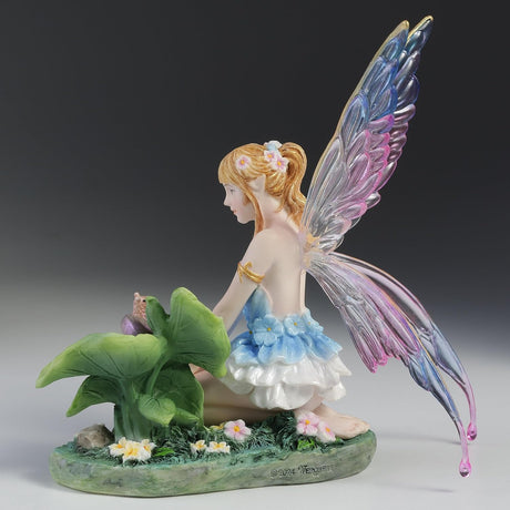 Blond fairy figurine with colorful wings sitting on flowers and grass with a snail on a leaf next to her