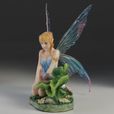 Blond fairy figurine with colorful wings sitting on flowers and grass with a snail on a leaf next to her