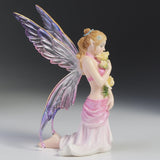 Fairy figurine with colorful wings and a pink dress holding flowers on a gray background