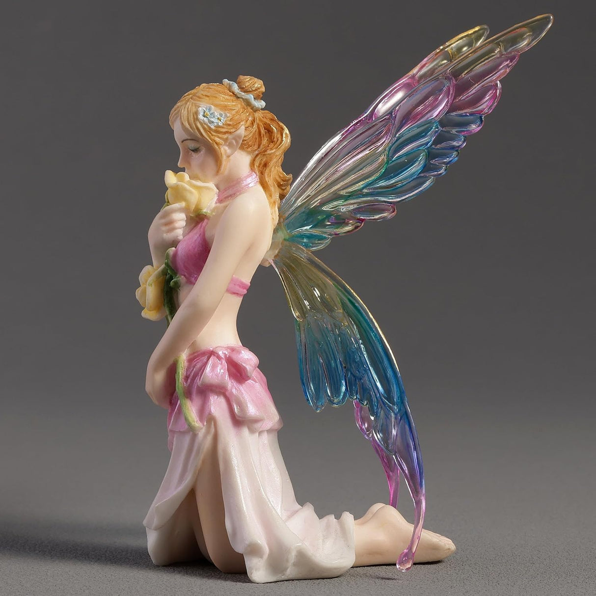 Fairy figurine with colorful wings holding a flower on a gray background
